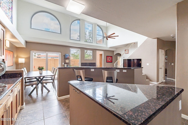 4296 N Rillito Creek Pl, Tucson, AZ 85719 - kitchen with a kitchen island, arched walkways, a ceiling fan, dark stone counters, and a towering ceiling