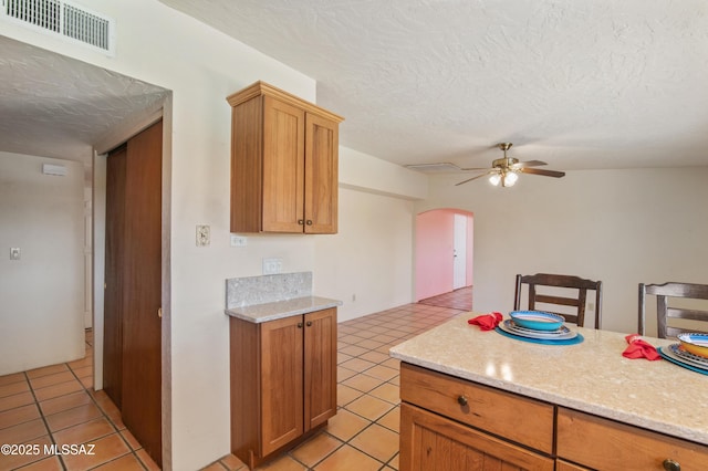 2831 W Puccini Pl, Tucson, AZ 85741 - kitchen featuring arched walkways, light tile patterned floors, a ceiling fan, a textured ceiling, and brown cabinetry