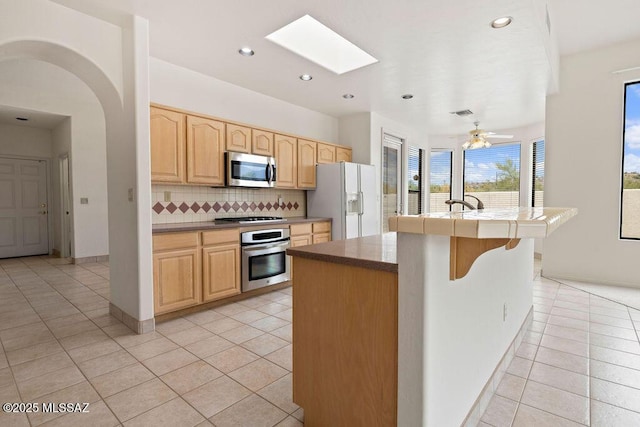 11126 N Guava Dr, Oro Valley, AZ 85737 - kitchen with stainless steel appliances, light brown cabinets, light tile patterned floors, tasteful backsplash, and a skylight