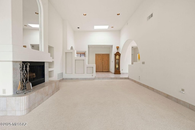 11126 N Guava Dr, Oro Valley, AZ 85737 - unfurnished living room with arched walkways, carpet floors, a towering ceiling, built in features, and a tile fireplace