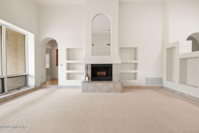 11126 N Guava Dr, Oro Valley, AZ 85737 - unfurnished living room featuring a high ceiling, carpet flooring, built in shelves, baseboards, and arched walkways