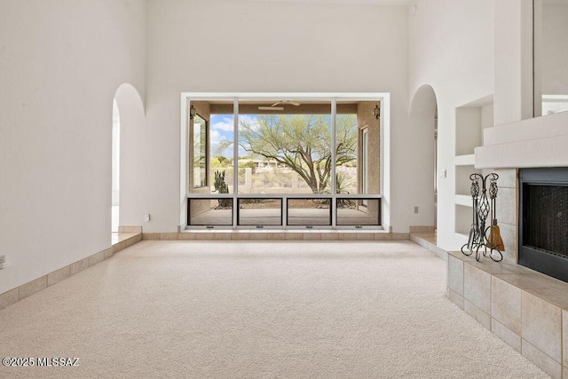 11126 N Guava Dr, Oro Valley, AZ 85737 - unfurnished living room featuring a high ceiling, arched walkways, a tile fireplace, and carpet floors