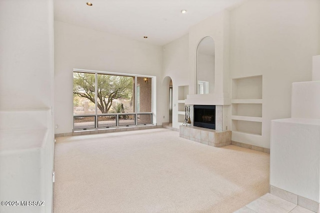 11126 N Guava Dr, Oro Valley, AZ 85737 - unfurnished living room with carpet floors, arched walkways, built in shelves, a fireplace, and a high ceiling
