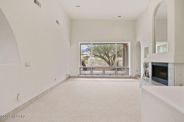 11126 N Guava Dr, Oro Valley, AZ 85737 - unfurnished living room featuring carpet floors, a tile fireplace, arched walkways, a towering ceiling, and recessed lighting