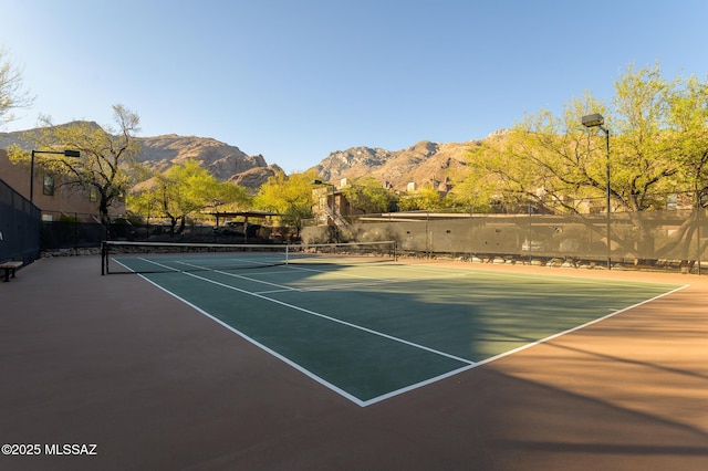 view of tennis court with a mountain view and fence