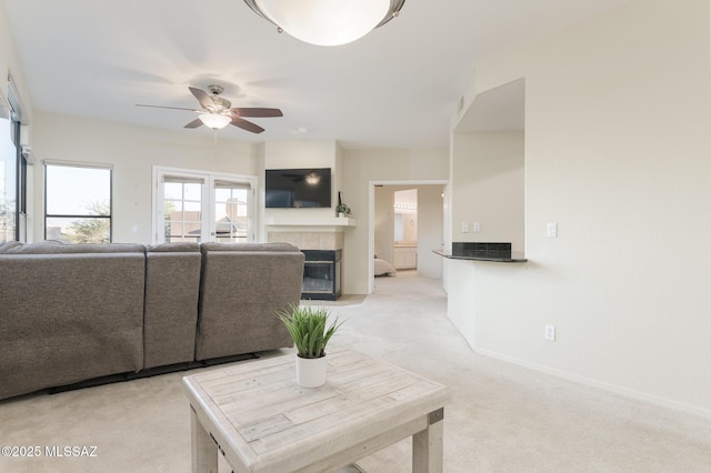 living room featuring light carpet, a ceiling fan, a tiled fireplace, and baseboards
