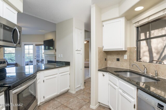 kitchen featuring appliances with stainless steel finishes, a sink, white cabinets, dark stone counters, and tasteful backsplash