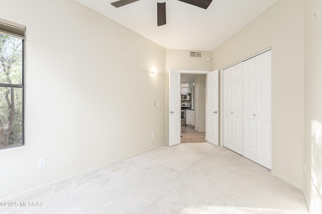 unfurnished bedroom with light colored carpet, a closet, a ceiling fan, and baseboards