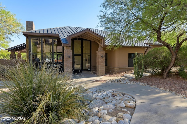 view of front of home with a standing seam roof, metal roof, a chimney, stucco siding, and stone siding