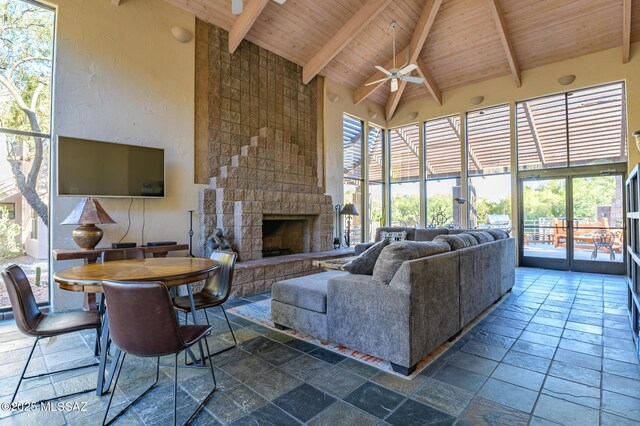 living room featuring wood ceiling, stone tile floors, ceiling fan, beam ceiling, and a stone fireplace
