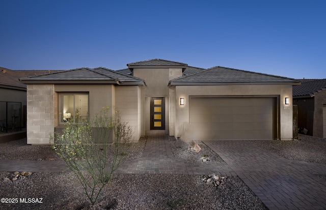 prairie-style house featuring an attached garage, stucco siding, a tile roof, and decorative driveway
