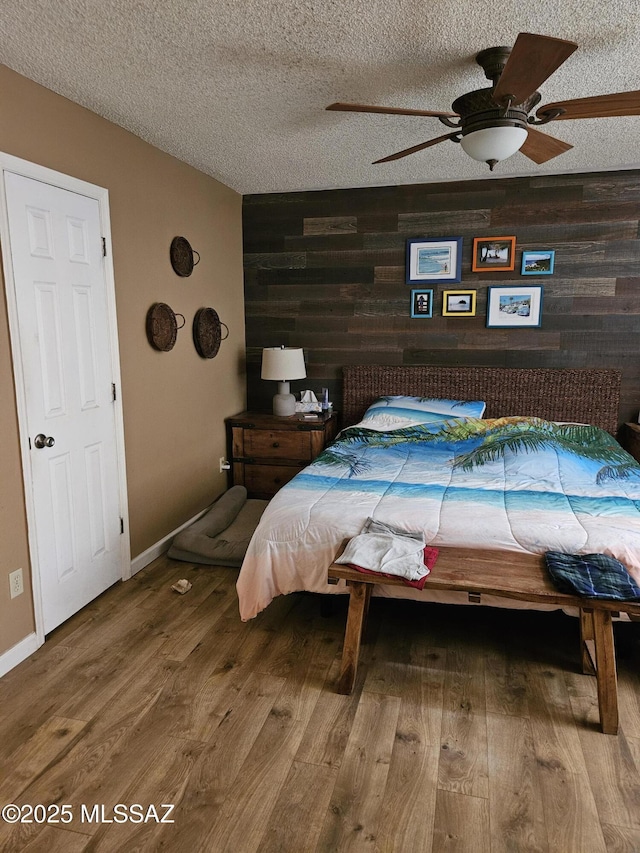 bedroom featuring wood walls, wood finished floors, an accent wall, a textured ceiling, and a ceiling fan