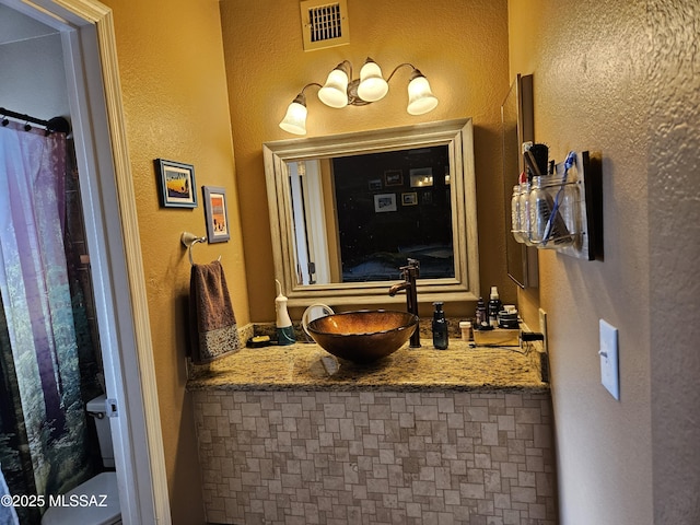 bathroom featuring toilet, vanity, and a textured wall