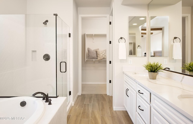 full bath with a stall shower, a walk in closet, a garden tub, double vanity, and baseboards