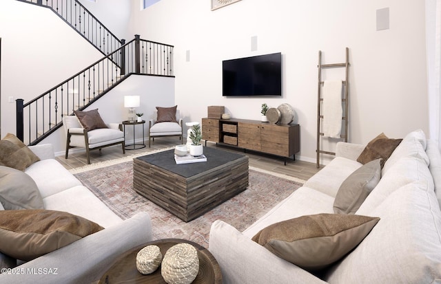 living area with wood finished floors, baseboards, a towering ceiling, and stairway