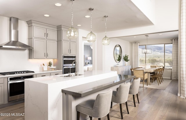 kitchen featuring wall chimney range hood, gas cooktop, stainless steel double oven, recessed lighting, and light wood-type flooring