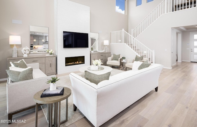 living area featuring a high ceiling, stairway, a fireplace, baseboards, and light wood finished floors
