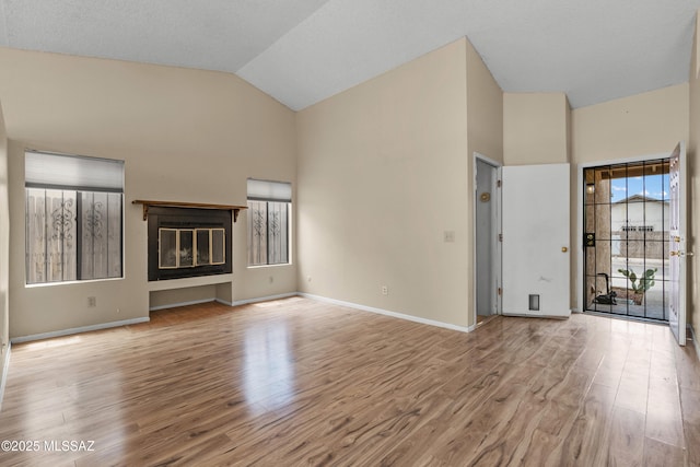 4765 S Windrose Dr, Tucson, AZ 85730 - unfurnished living room with high vaulted ceiling, wood finished floors, baseboards, and a glass covered fireplace