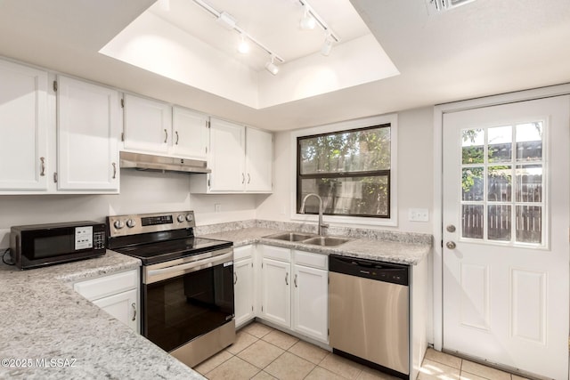 kitchen with appliances with stainless steel finishes, under cabinet range hood, a sink, rail lighting, and light tile patterned flooring