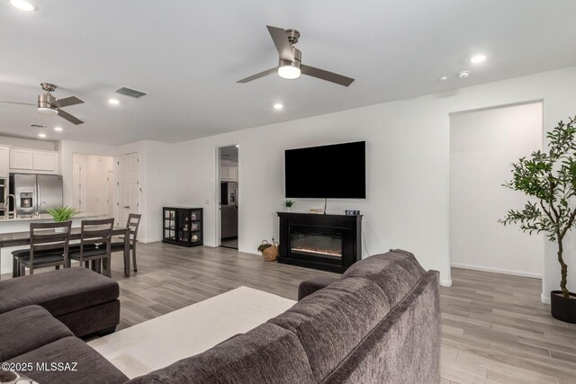 7988 S Bonanza Park Dr, Tucson, AZ 85747 - living area with a ceiling fan, light wood-style flooring, recessed lighting, a glass covered fireplace, and baseboards
