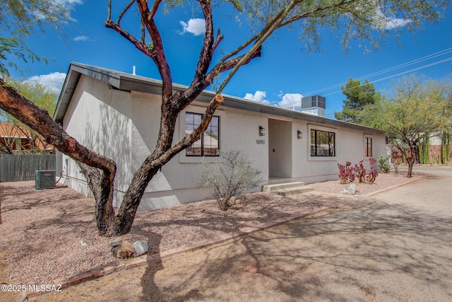 view of front of home with stucco siding, fence, and cooling unit