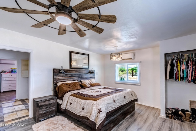 bedroom featuring a wall mounted air conditioner, light wood-style flooring, and baseboards