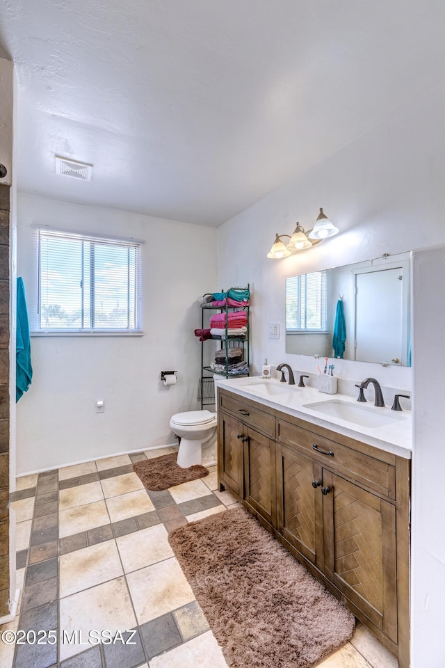 bathroom with plenty of natural light, double vanity, and toilet
