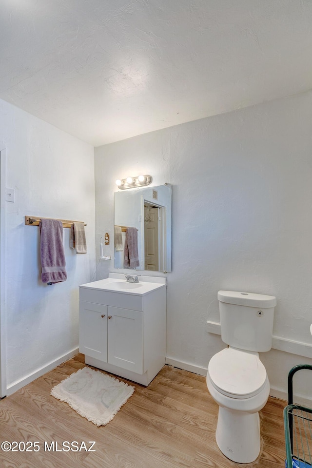 bathroom featuring wood finished floors, toilet, vanity, and baseboards