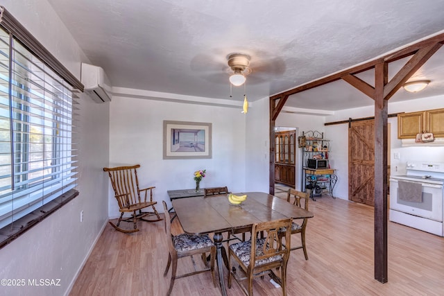 dining area featuring a barn door, a wall mounted air conditioner, a ceiling fan, light wood-style flooring, and baseboards