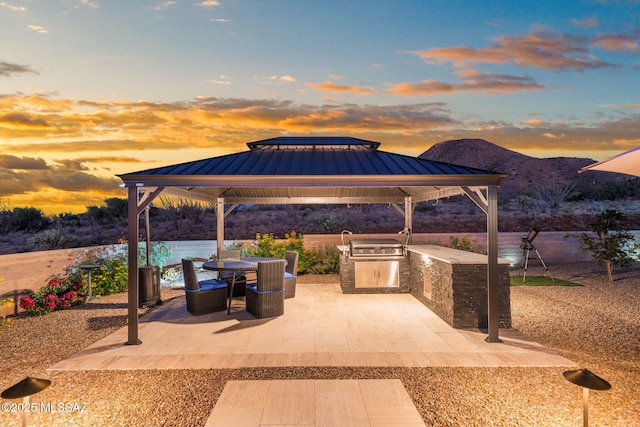 10465 E Ocotillo Rim Trl, Vail, AZ 85641 - patio terrace at dusk with a gazebo, an outdoor kitchen, a mountain view, and outdoor dining area