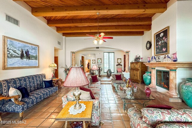 living area with arched walkways, a ceiling fan, wood ceiling, beam ceiling, and tile patterned floors