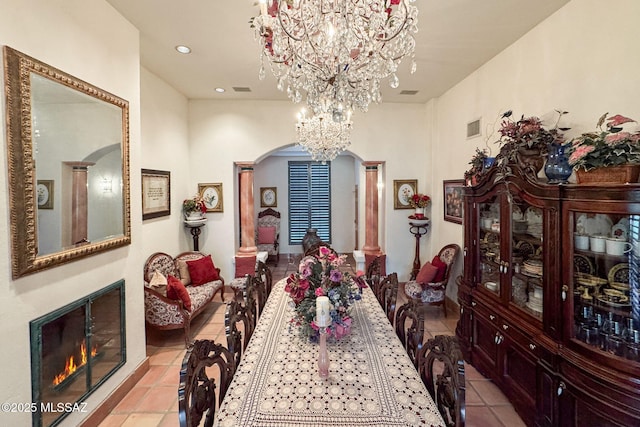 dining area featuring arched walkways, a chandelier, light tile patterned floors, a warm lit fireplace, and recessed lighting