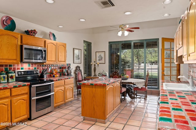 kitchen with appliances with stainless steel finishes, tile countertops, a sink, tasteful backsplash, and recessed lighting