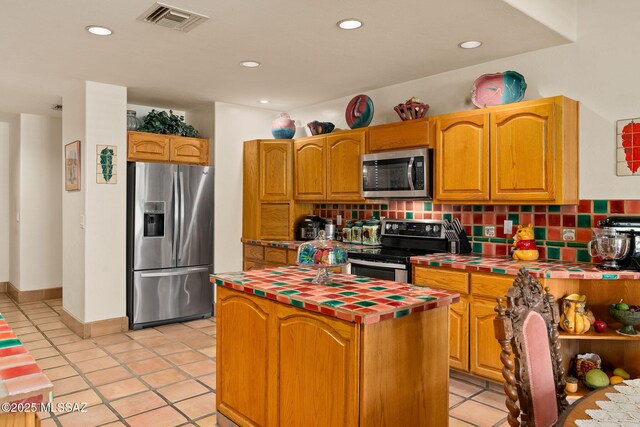kitchen with stainless steel appliances, tile counters, a center island, backsplash, and light tile patterned floors