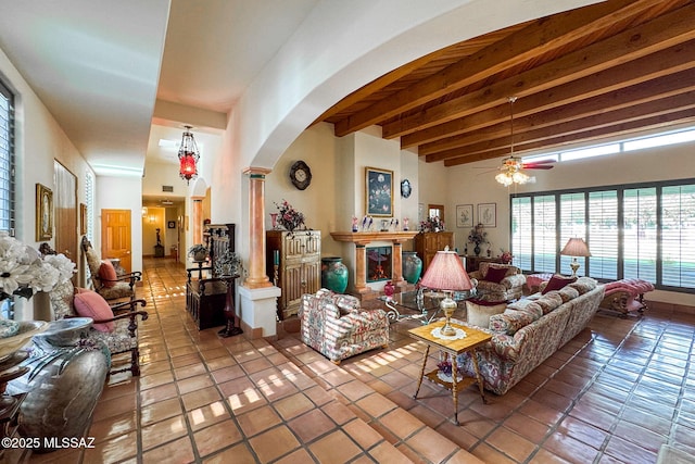 living room featuring arched walkways, tile patterned flooring, ceiling fan, beamed ceiling, and decorative columns