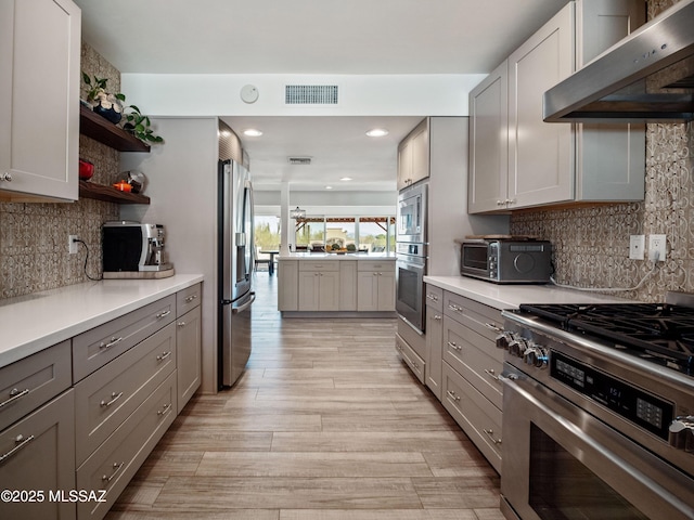 5825 N Camino Miraval Dr, Tucson, AZ 85718 - kitchen with appliances with stainless steel finishes, under cabinet range hood, gray cabinetry, open shelves, and light wood-style floors