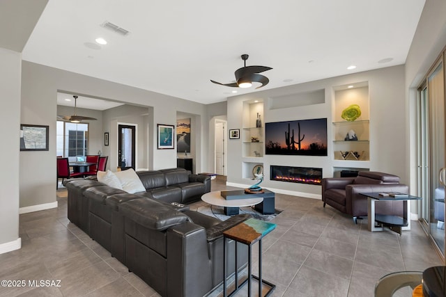66450 E Sundance Pl, Saddlebrooke, AZ 85739 - living area featuring ceiling fan, built in shelves, tile patterned flooring, baseboards, and a glass covered fireplace