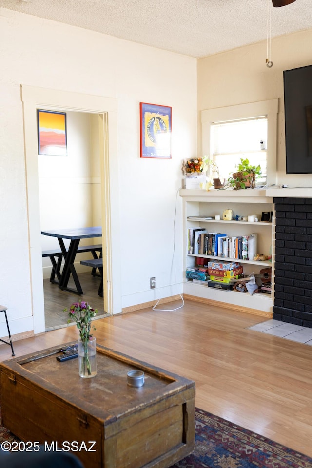 616 E 8th St, Tucson, AZ 85705 - living room featuring wood finished floors, a textured ceiling, a brick fireplace, and baseboards