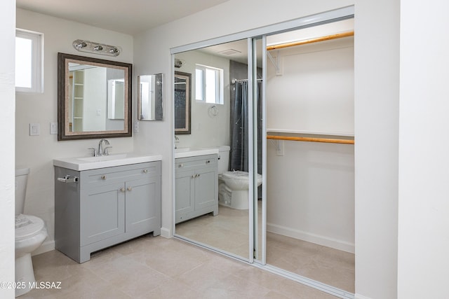 full bath with toilet, vanity, tile patterned floors, a walk in closet, and baseboards
