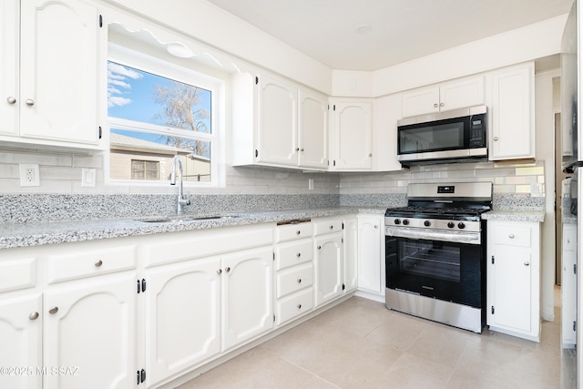 kitchen featuring appliances with stainless steel finishes, a sink, white cabinets, light tile patterned floors, and tasteful backsplash