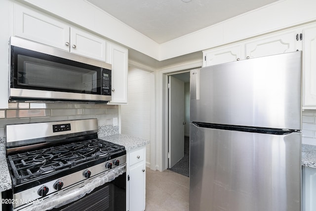 kitchen featuring appliances with stainless steel finishes, white cabinets, backsplash, and light stone counters