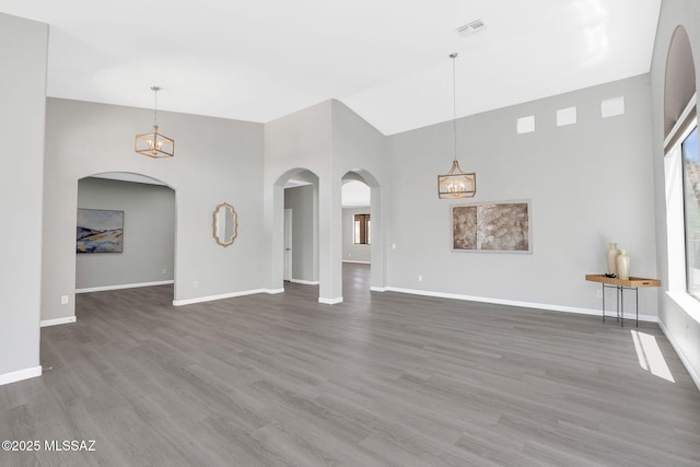 63370 E Whispering Tree Ln, Saddlebrooke, AZ 85739 - unfurnished living room with arched walkways, high vaulted ceiling, wood finished floors, baseboards, and healthy amount of natural light