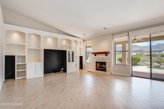 36359 S Wind Crest Dr, Saddlebrooke, AZ 85739 - unfurnished living room featuring a mountain view, a tile fireplace, light wood finished floors, built in features, and vaulted ceiling