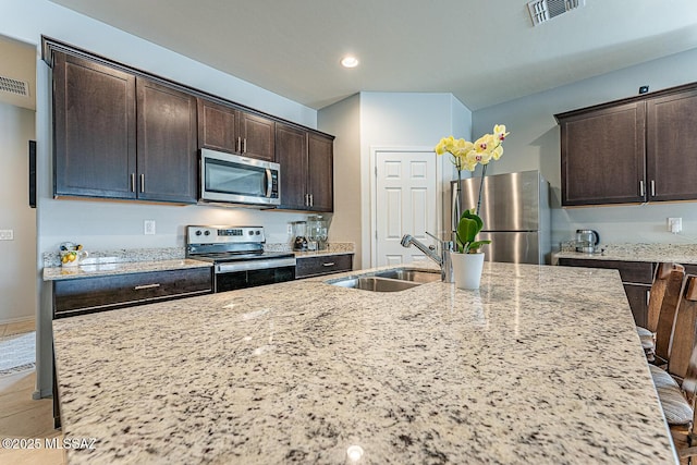 12625 N Wildrose Dr, Marana, AZ 85653 - kitchen featuring appliances with stainless steel finishes, a sink, dark brown cabinetry, light stone countertops, and a center island with sink