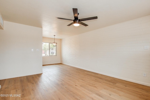 spare room with brick wall, ceiling fan, light wood finished floors, a chandelier, and baseboards
