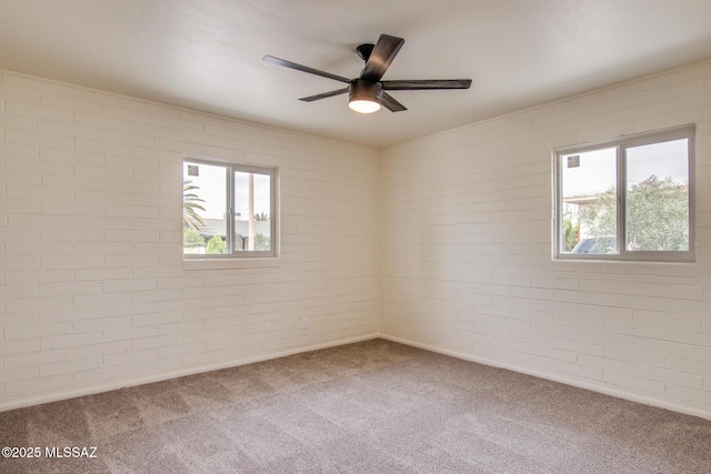 carpeted spare room with plenty of natural light, ceiling fan, and brick wall