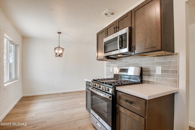 kitchen with stainless steel appliances, light wood-style flooring, light countertops, brick wall, and baseboards