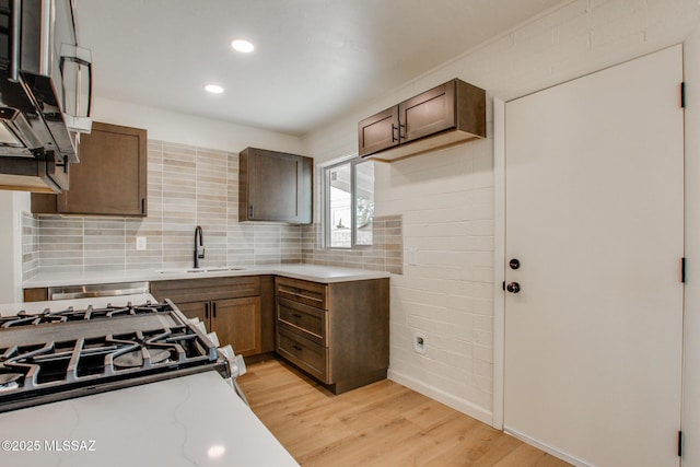 kitchen featuring a sink, light countertops, backsplash, light wood-type flooring, and baseboards