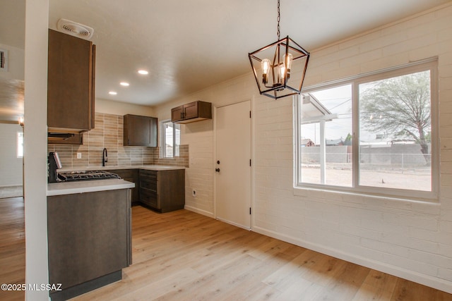 kitchen with a chandelier, light wood-style floors, light countertops, baseboards, and backsplash
