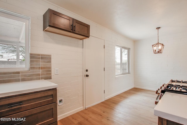 kitchen with light wood-type flooring, light countertops, brick wall, baseboards, and pendant lighting